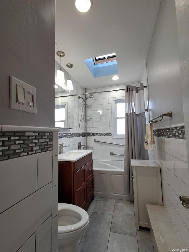 full bathroom with a skylight, tile patterned floors, shower / bath combo with shower curtain, tile walls, and toilet