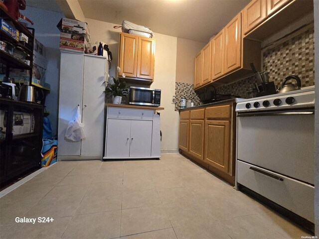 607 Ashford St, Brooklyn, NY 11207 - kitchen with stainless steel microwave, stove, tasteful backsplash, dark countertops, and light tile patterned floors
