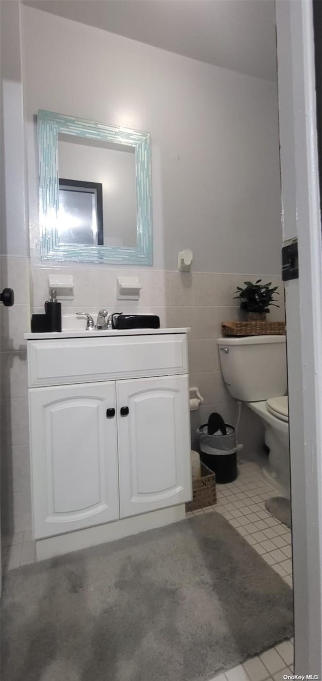 bathroom with toilet, vanity, tile patterned floors, and tile walls