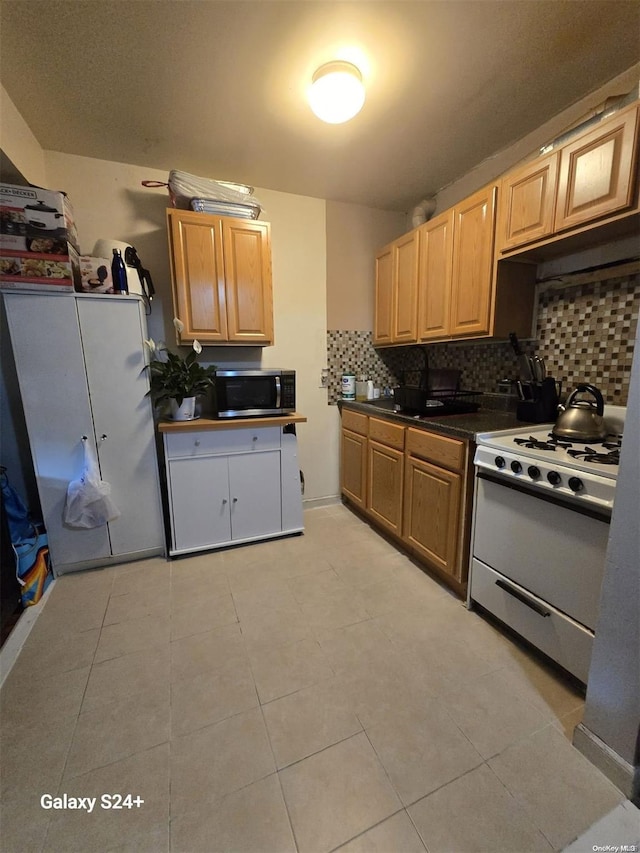 607 Ashford St, Brooklyn, NY 11207 - kitchen with white gas range, stainless steel microwave, tasteful backsplash, dark countertops, and light tile patterned floors