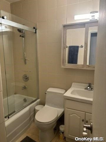 full bathroom with vanity, toilet, tile walls, and bath / shower combo with glass door