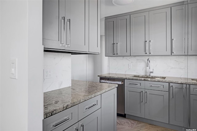 kitchen with backsplash, light stone counters, stainless steel dishwasher, gray cabinetry, and sink