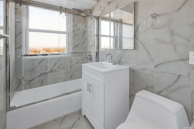 full bathroom featuring vanity, toilet, bath / shower combo with glass door, and tile walls