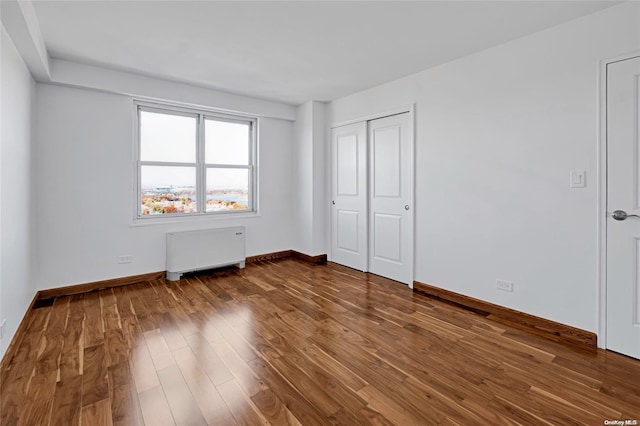 unfurnished bedroom featuring hardwood / wood-style floors, radiator, and a closet