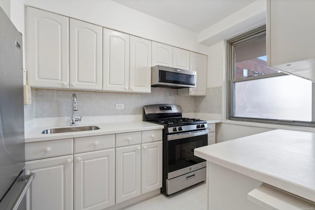 kitchen featuring appliances with stainless steel finishes, tasteful backsplash, sink, light tile patterned floors, and white cabinets