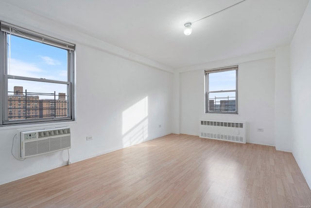 unfurnished room featuring radiator heating unit, light hardwood / wood-style flooring, and a wall mounted AC