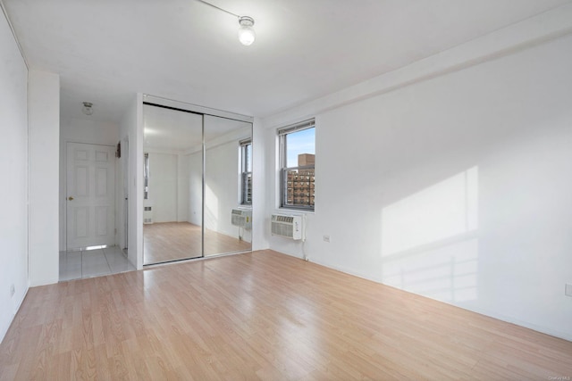 unfurnished bedroom with light hardwood / wood-style floors, a wall unit AC, and a closet