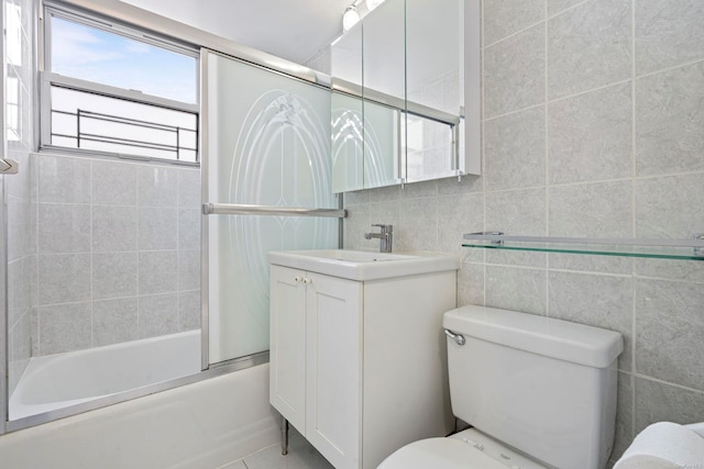 full bathroom featuring combined bath / shower with glass door, vanity, toilet, and tile walls