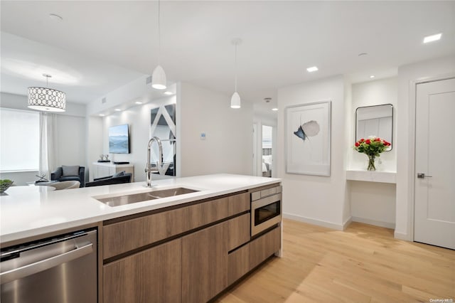 kitchen featuring decorative light fixtures, sink, light wood-type flooring, and stainless steel appliances