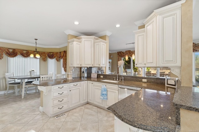 kitchen featuring kitchen peninsula, hanging light fixtures, dark stone counters, light tile patterned flooring, and sink