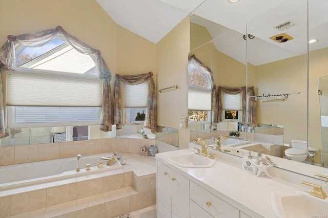 bathroom featuring toilet, vanity, a relaxing tiled tub, and plenty of natural light