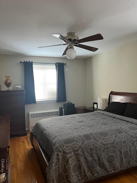 bedroom featuring dark hardwood / wood-style flooring, radiator heating unit, and ceiling fan