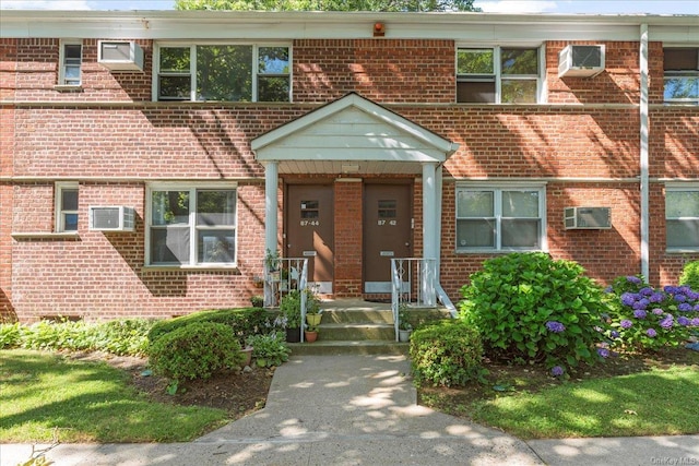 view of front facade with brick siding and a wall mounted air conditioner