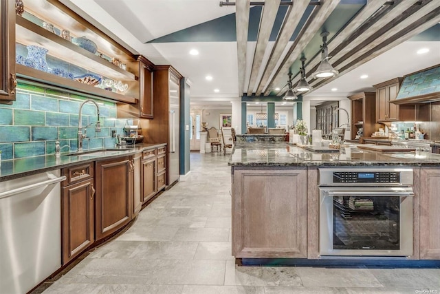 kitchen featuring decorative backsplash, appliances with stainless steel finishes, sink, dark stone countertops, and hanging light fixtures