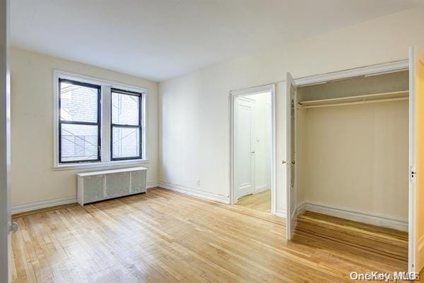 unfurnished bedroom with a closet, light hardwood / wood-style flooring, and radiator heating unit