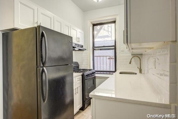 kitchen with black gas range, white cabinets, sink, decorative backsplash, and stainless steel fridge