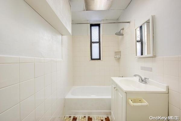 bathroom with tiled shower / bath combo, tile walls, and vanity