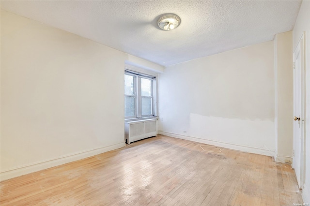 empty room with radiator, light hardwood / wood-style flooring, and a textured ceiling