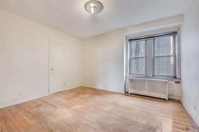 empty room featuring radiator heating unit, a textured ceiling, and light hardwood / wood-style flooring