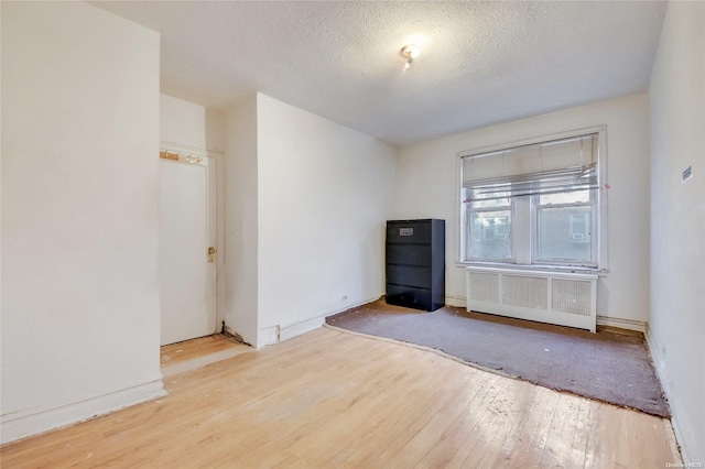 empty room featuring a textured ceiling, radiator, and light hardwood / wood-style flooring