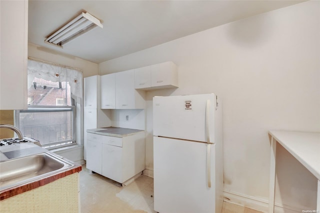 kitchen with white fridge, white cabinetry, and sink