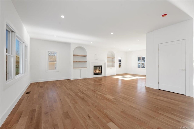 unfurnished living room with plenty of natural light, built in features, and light hardwood / wood-style flooring