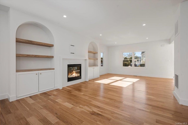 unfurnished living room featuring built in shelves and light wood-type flooring