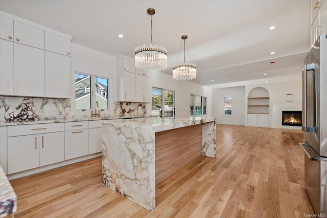 kitchen featuring light stone countertops, backsplash, a kitchen island, pendant lighting, and white cabinetry