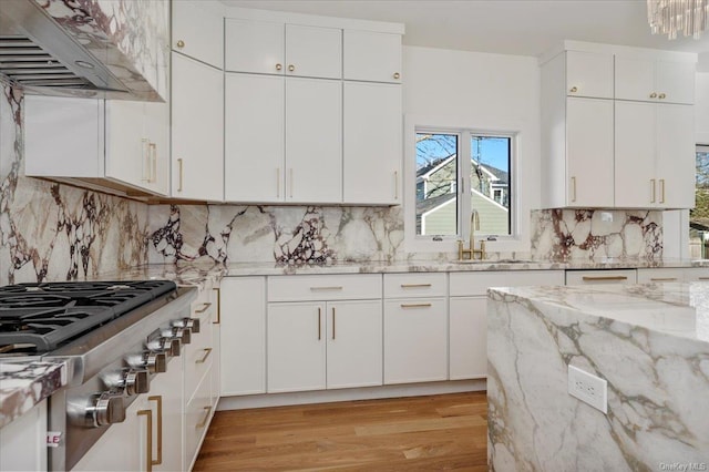 kitchen featuring light stone countertops, cooktop, sink, wall chimney range hood, and white cabinets