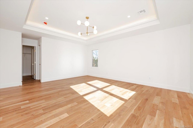 spare room featuring a tray ceiling, light hardwood / wood-style flooring, and a chandelier