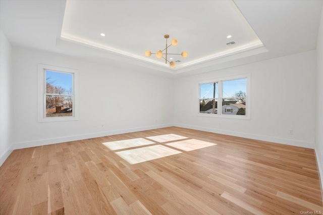 empty room with light wood-type flooring, an inviting chandelier, and a raised ceiling