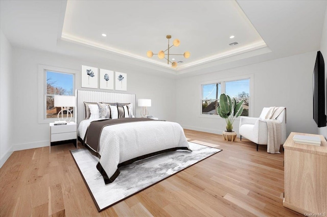 bedroom featuring an inviting chandelier, a tray ceiling, and light hardwood / wood-style flooring