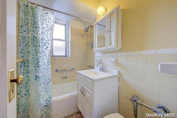 full bathroom with shower / bath combo, toilet, tile walls, and vanity