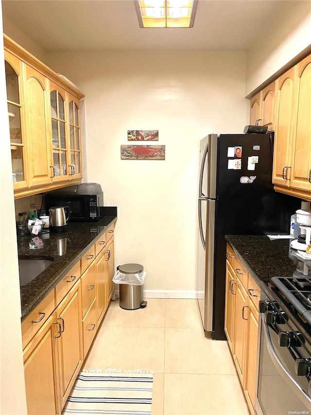 kitchen with appliances with stainless steel finishes, sink, dark stone counters, and light tile patterned flooring