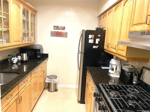 kitchen with exhaust hood, stainless steel range with gas cooktop, sink, dark stone countertops, and light tile patterned floors