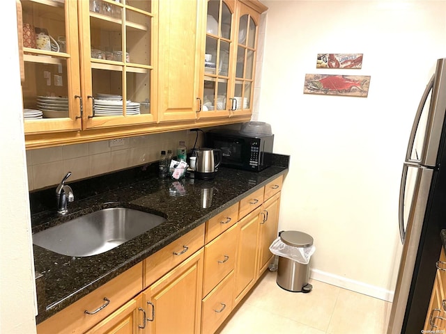 kitchen featuring backsplash, dark stone counters, sink, light tile patterned flooring, and stainless steel refrigerator