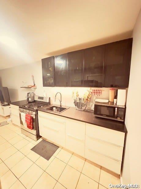 kitchen featuring appliances with stainless steel finishes, light tile patterned floors, white cabinetry, and sink