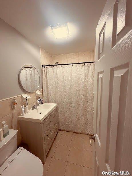 bathroom with tile patterned flooring, vanity, toilet, and tile walls