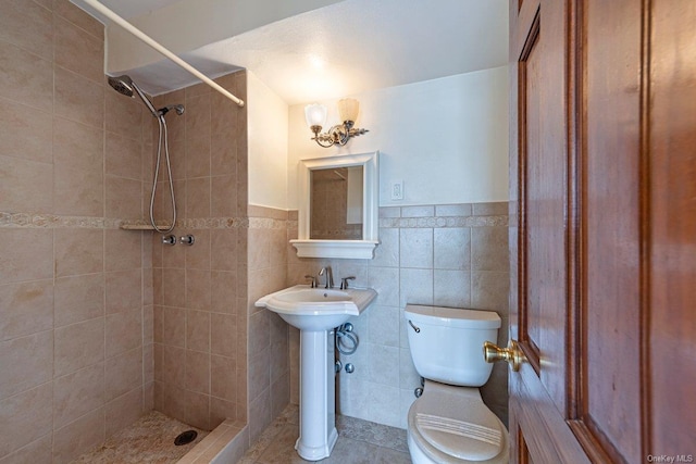 bathroom with sink, tile patterned flooring, toilet, tiled shower, and tile walls