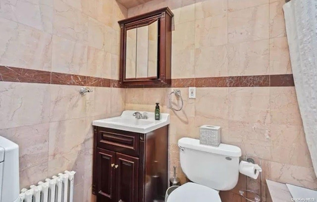 bathroom with radiator heating unit, vanity, tile walls, and toilet