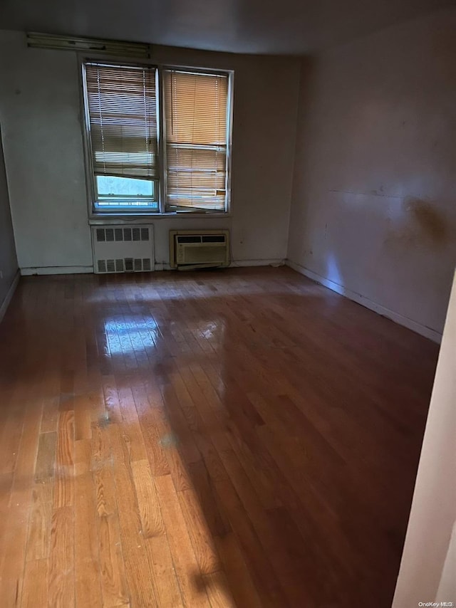 empty room featuring radiator heating unit, light hardwood / wood-style flooring, and a wall mounted AC