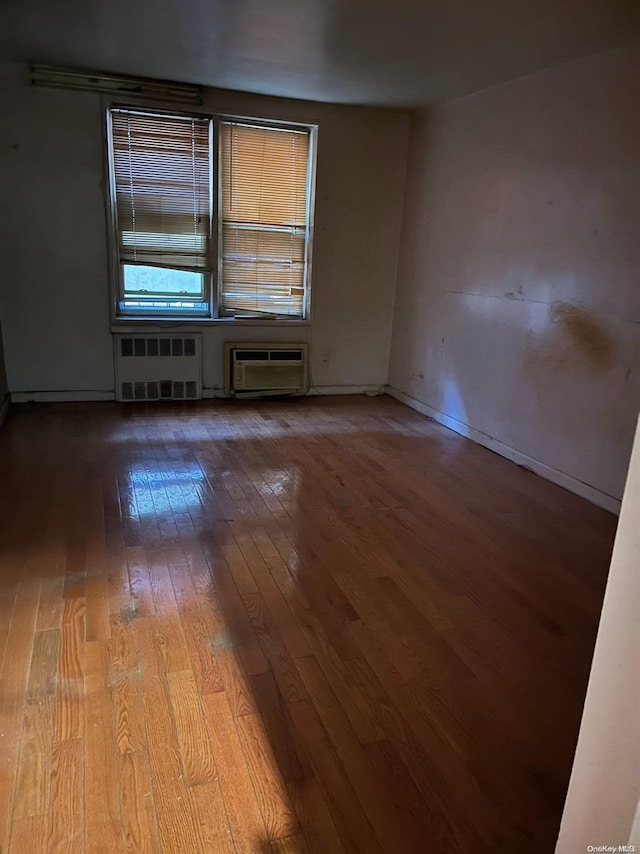 spare room with a wall mounted air conditioner, radiator heating unit, and light hardwood / wood-style flooring