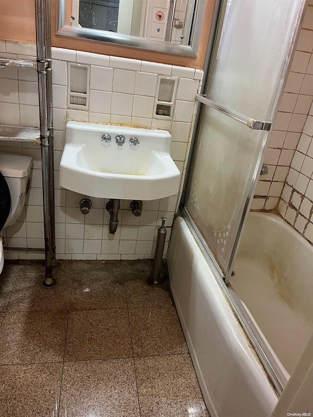 full bathroom featuring sink, toilet, bath / shower combo with glass door, and tile walls