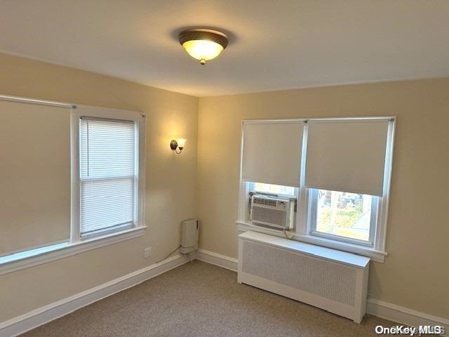 spare room with radiator heating unit, cooling unit, and light colored carpet