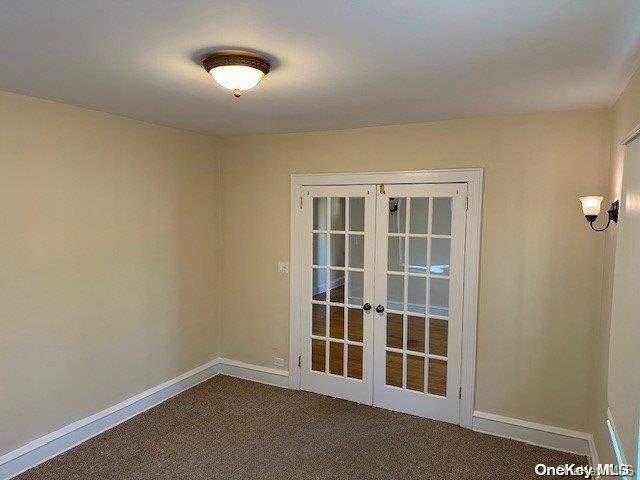 spare room featuring dark colored carpet and french doors