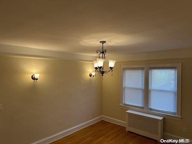 unfurnished room featuring hardwood / wood-style flooring, a notable chandelier, and radiator