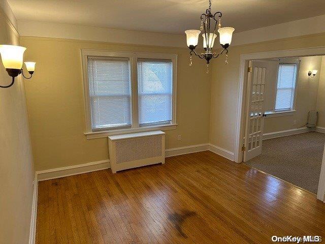 unfurnished dining area featuring hardwood / wood-style floors, radiator heating unit, and an inviting chandelier