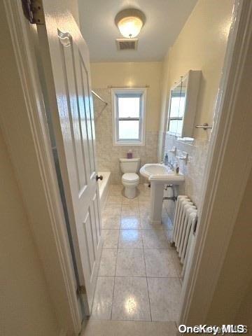 full bathroom with radiator, tile patterned flooring, tile walls, and toilet