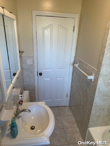 bathroom featuring a tub to relax in, sink, tile walls, and tile patterned flooring