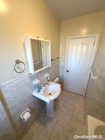 bathroom with tile patterned floors, radiator, a bathtub, sink, and tile walls